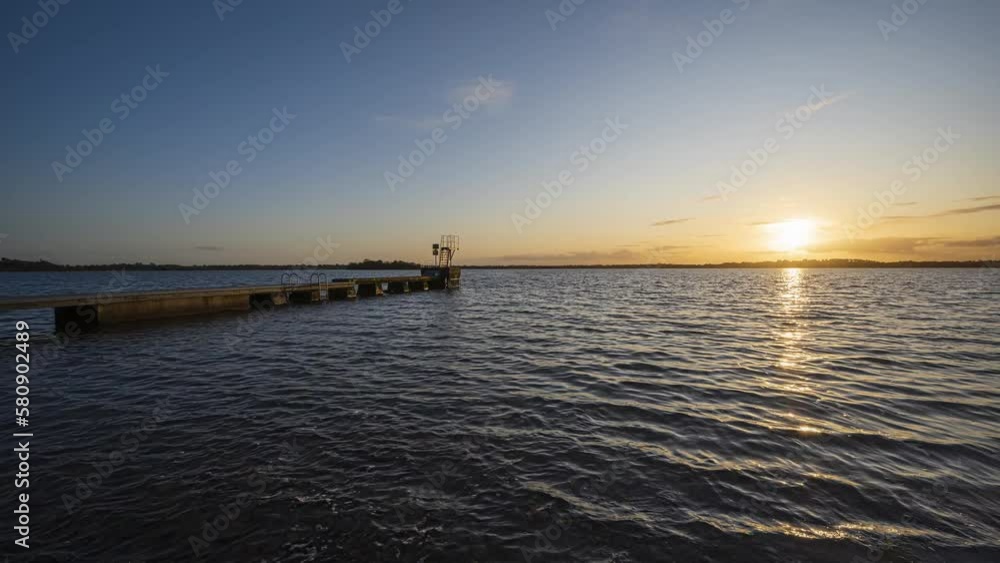 Panorama motion timelapse of local lake with few people on concrete jetty in county Westmeath in Ireland during sunset with clouds above the horizon. Panorama motion timelapse of local lake with few people on concrete jetty in county Westmeath in Ireland during sunset with clouds above the horizon.