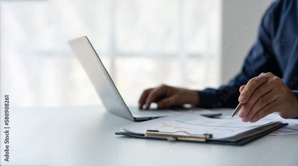 young business man Recording data on laptop, comparing details from graphs. Business income charts in the areas of real estate, tax, management, technology marketing in a private office. young business man Recording data on laptop, comparing details from graphs. Business income charts in the areas of real estate, tax, management, technology marketing in a private office.