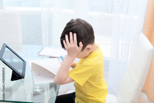 School boy in yellow t-shirt sitting at the table with digital tablet studying at home. Distance learning online education concept