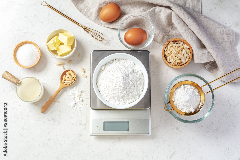Flour in white bowl measuring on digital scale with baking ingredients and  utensil on marble kitchen table Stock Photo