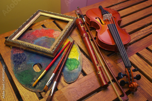 Music and painting, Art attributes. Violin, bow, pipe, art palette, brushes, picture frame on a wooden table.