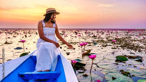 Asian women with a hat and dress in a boat at the Beautiful Red Lotus Sea Kumphawapi is full of pink flowers in Udon Thani in northern Thailand. Flora of Southeast Asia. photo