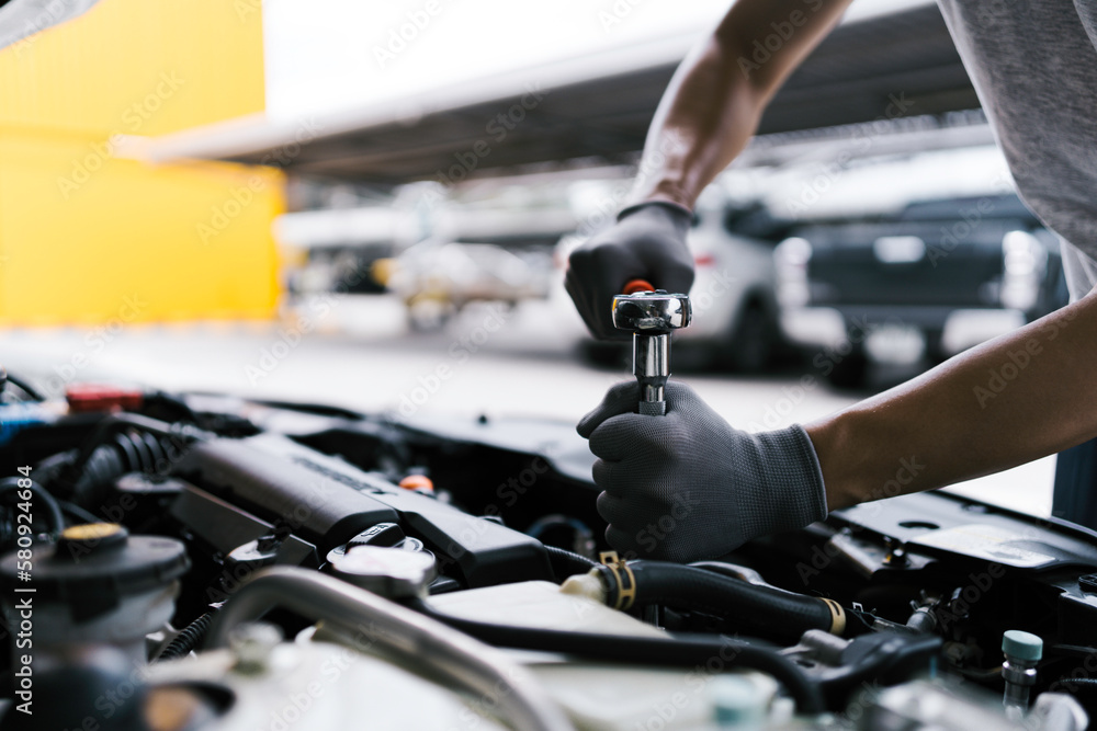 Professional car mechanic using a wrench for working on the engine of the car in the garage for car auto repair service and maintenance check concept for the car before leaving. Professional car mechanic using a wrench for working on the engine of the car in the garage for car auto repair service and maintenance check concept for the car before leaving.