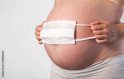 A pregnant girl holds a protective medical mask against the background of her belly. The concept of protection against respiratory diseases coronavirus and influenza in pregnant women.  photo