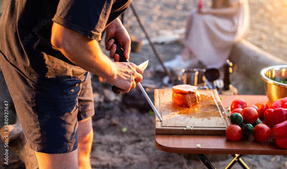 sharpening a knife in nature at a picnic for cooking. Camping. Fresh  vegetables on the table, bushcraft Stock Photo