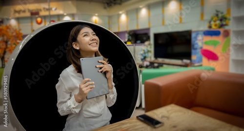 Beautiful asian businesswoman is overjoyed when she gets promoted by her boss via tablet with a smile while sitting on a modern round chair in the living room.