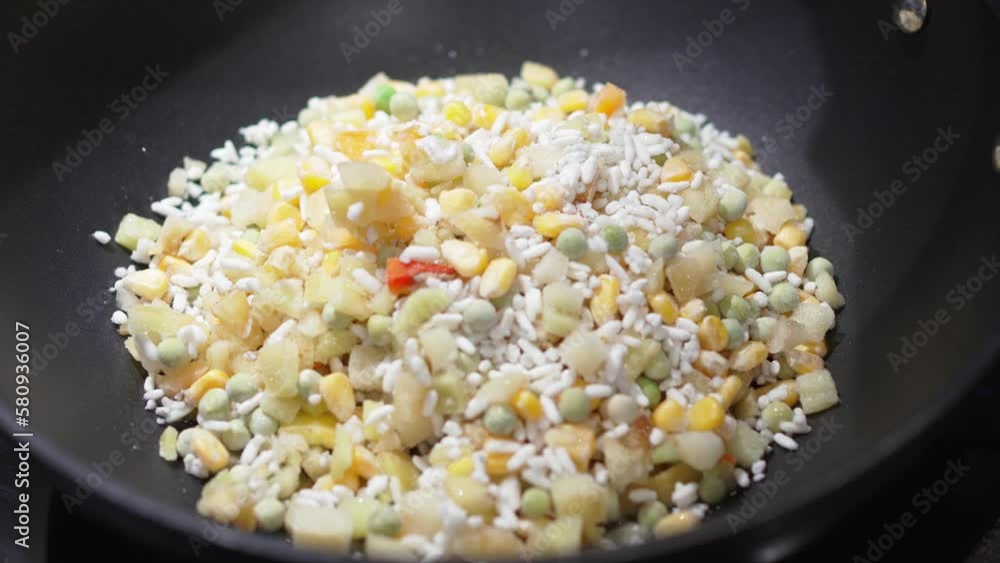 frozen vegetable mixture with rice is fried in a frying pan. frozen vegetable mixture with rice is fried in a frying pan.