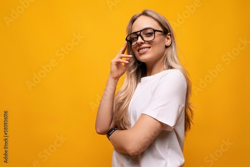 smart smiling blond woman with poor eyesight wearing glasses on yellow background