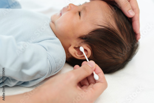 close up mother using cotton bud to cleaning ear of newborn baby on bed