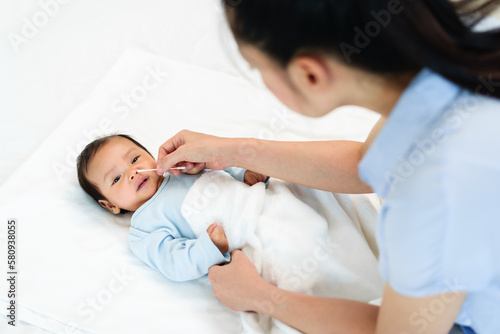 mother using cotton bud to clean nose of newborn baby on bed