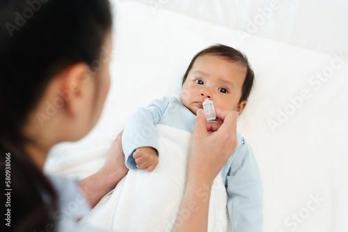 newborn baby gets nose drops by mother on bed