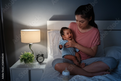 Fotografie mother holding burping and crying baby after feeding milk on bed at night