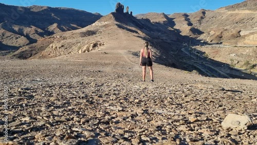 young woman observes the rock formation called el camel, near the beach of Medio Almud on the island of Gran Canaria on a sunny day. photo