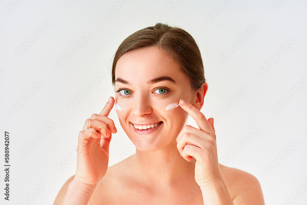 Fototapeta premium Portrait of young woman applying facial cream for beautiful healthy skin on white background
