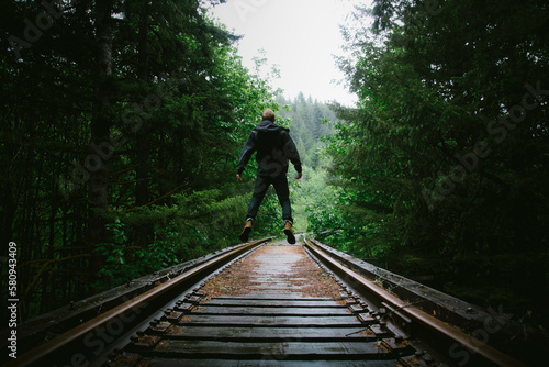 Rear view of man jumping on railway tracks amidst trees photo