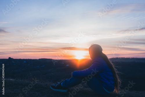 Fototapeta Naklejka Na Ścianę i Meble -  A young girl on the background of the sunset. Evening in nature in the mountains. Prayer against the background of the sky.