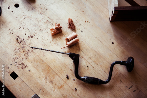 High angle view of hand drill by sawdust on wooden table in workshop