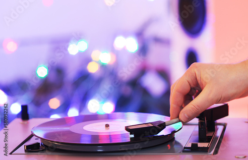 A hand puts a record on a vintage turntable against the background of lights.