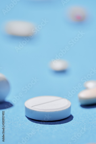 Medicine and drug concept. Close up shot of white pill on blue background with different tablets on it out of focus.