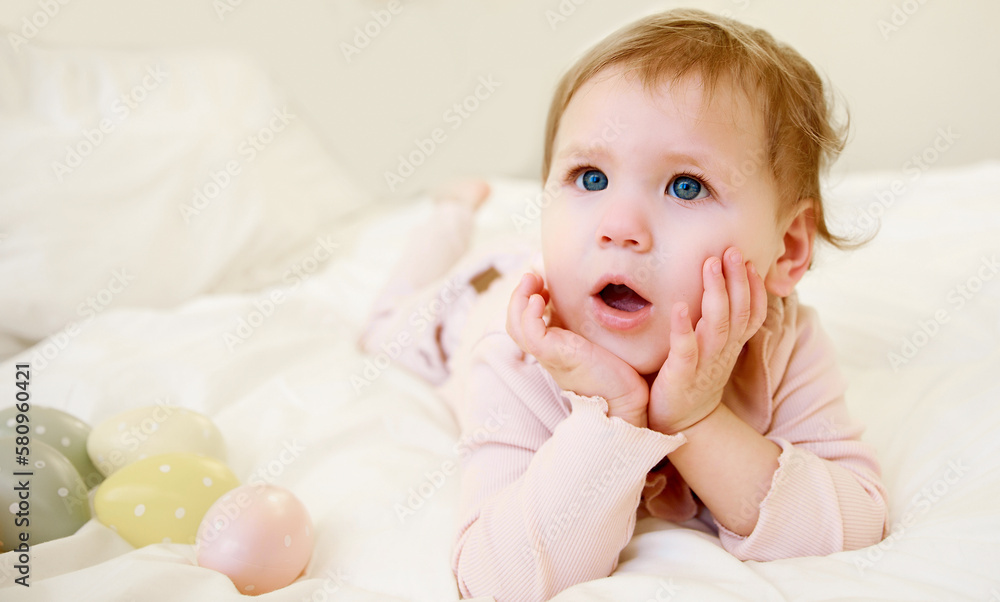 A cute little girl lies in a crib and props her head up with her hands. Easter eggs lie next to the children. Happy easter. 1 year old girl.
A cute little girl lies in a crib and props her head up with her hands. Easter eggs lie next to the children. Happy easter. 1 year old girl.