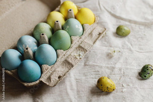 Stylish easter eggs and blooming cherry branch on rustic table. Happy Easter! Rustic easter still life. Natural painted eggs in paper tray and spring blossom on linen fabric