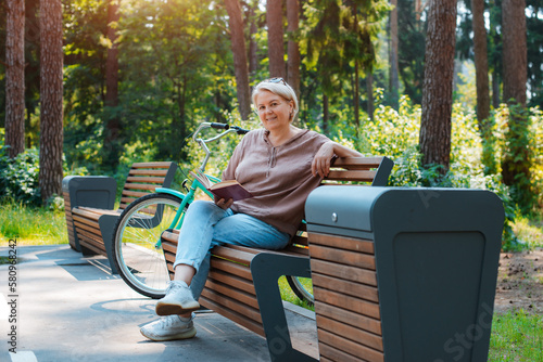 Dreamy modern old lady relaxing in city park. Pensive senior grey haired woman in casual sitting wooden bench outdoors.