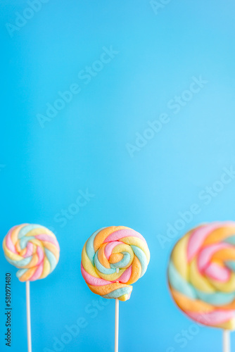 Colorful rainbow twist roll marshmallow like lollipop on blue background. Sweet food.