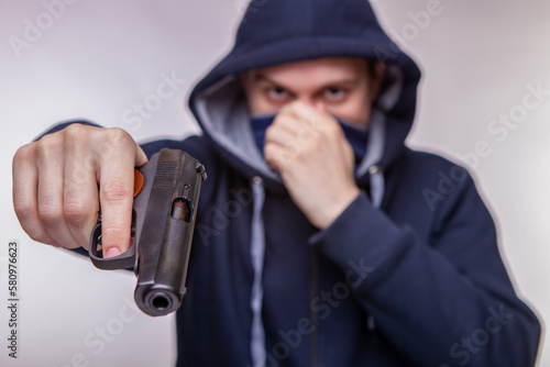 Hooded man holds hand gun and points it to the camera. Concept of crime and fire arm assault with mature man. Armed robbery on black, shallow depth of field, focus on the barrel of the pistol.
