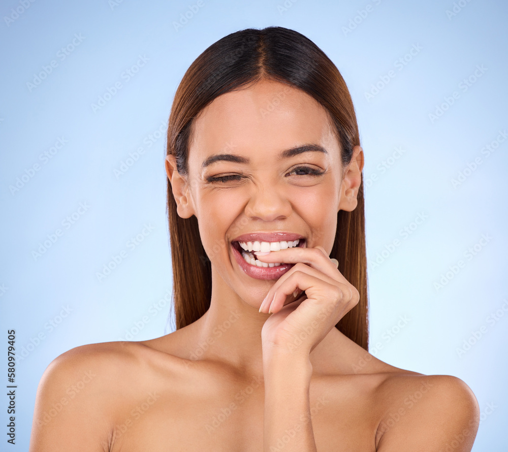 Beauty, woman and biting finger and wink portrait for skincare dermatology cosmetics in studio. Female model person on blue background for self care, facial glow and healthy or clean skin with smile Beauty, woman and biting finger and wink portrait for skincare dermatology cosmetics in studio. Female model person on blue background for self care, facial glow and healthy or clean skin with smile