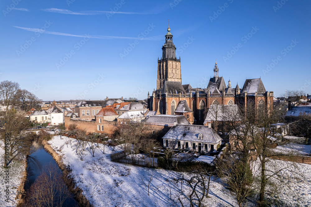 City garden of medieval Hanseatic Dutch tower town Zutphen in the Netherlands covered in snow with historic heritage wall and Walburgiskerk church rising above against a clear blue sky