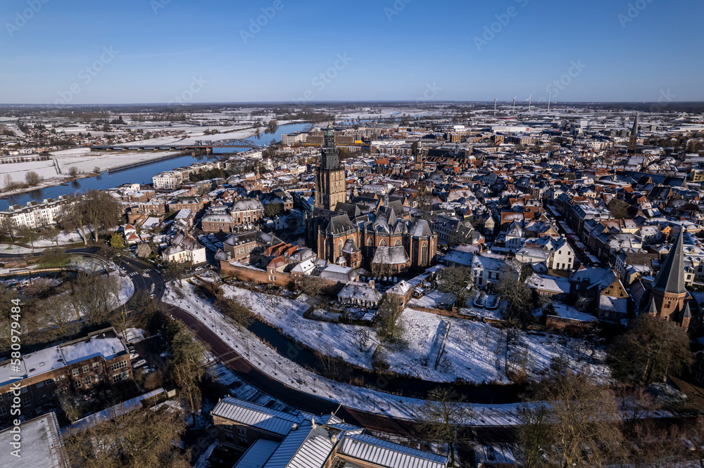 Canal surrounding medieval Hanseatic Dutch city wall of tower town Zutphen in the Netherlands covered in snow with historic heritage buildings and river IJssel passing by in the background