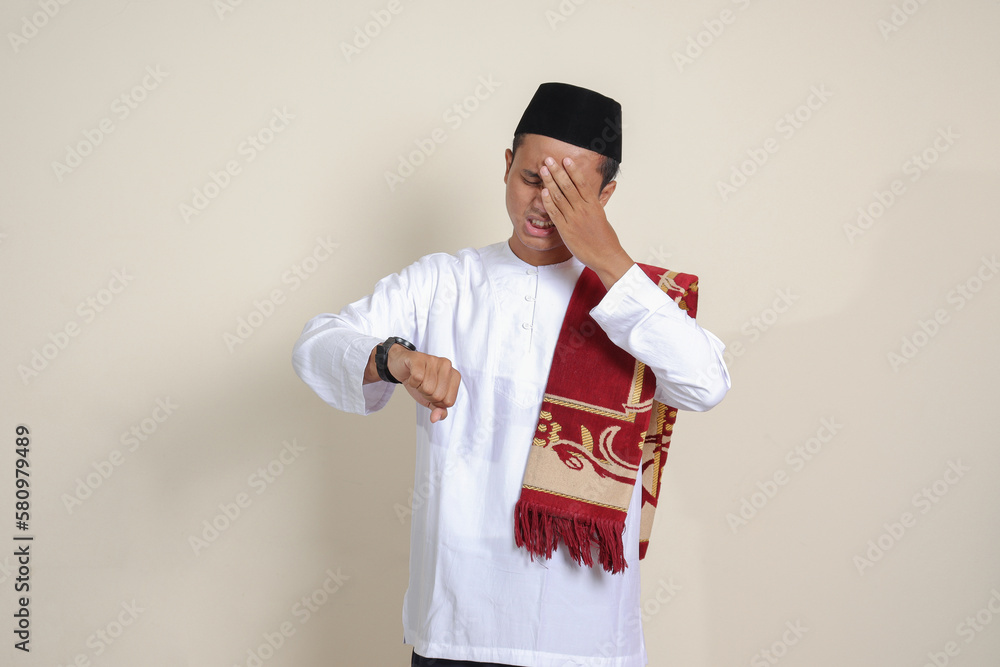 Portrait of attractive Asian muslim man in white shirt looking on wrist watch realizing that he is getting late for a meeting. Isolated image on gray background Portrait of attractive Asian muslim man in white shirt looking on wrist watch realizing that he is getting late for a meeting. Isolated image on gray background