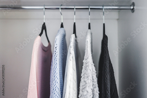 minimalist capsule wardrobe selection of womenswear sweaters and cardigans with matching hangers shot at shallow depth of field