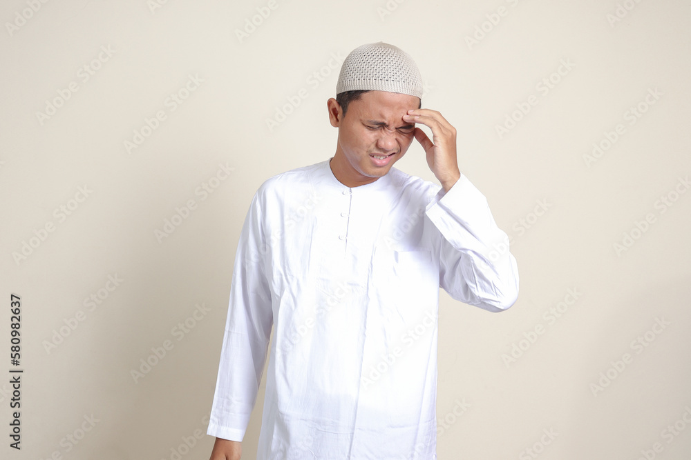 Portrait of attractive Asian muslim man in white shirt having a migraine, touching his temple. Headache disease concept. Isolated image on gray background
