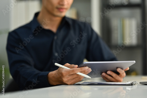 Selective focus on hands. Cropped image of businessman holding stylus pen and using digital tablet at office desk