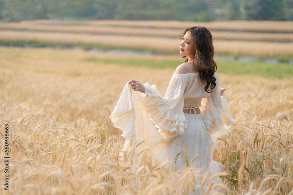 Beautiful Asian women were in white dresses relaxed and happy in the Barley rice field season golden color of the wheat plant. Freedom traveler, dreamy portrait in a wheat field.