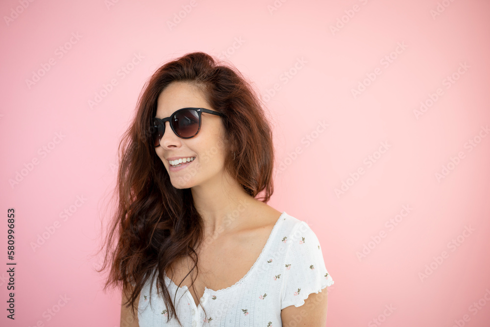 pretty young woman with black sunglasses and long hair with flowered shirt is standing in front of pink background pretty young woman with black sunglasses and long hair with flowered shirt is standing in front of pink background
