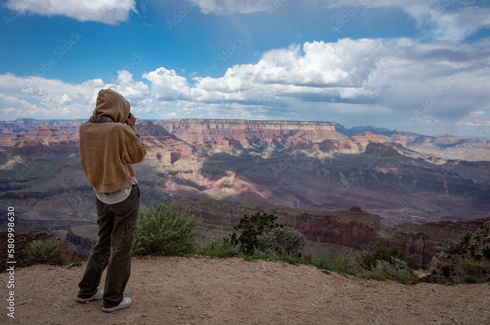 Naklejka premium Young girl with sweatshirt and hoodie taking photos of the landscape of the Grand Canyon, her back is turned
