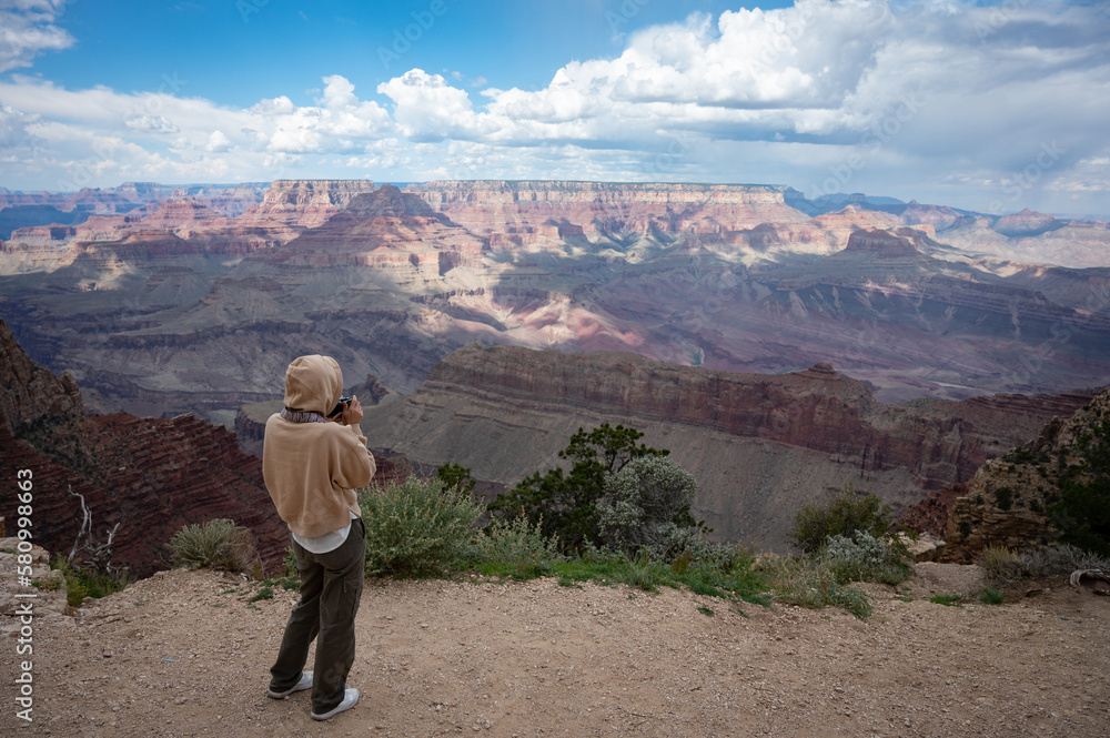 Young girl with sweatshirt and hoodie taking photos of the landscape of the Grand Canyon, her back is turned