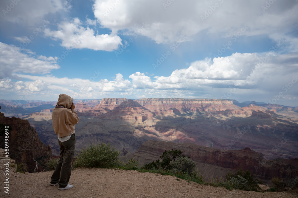 Young girl with sweatshirt and hoodie taking photos of the landscape of the Grand Canyon, her back is turned