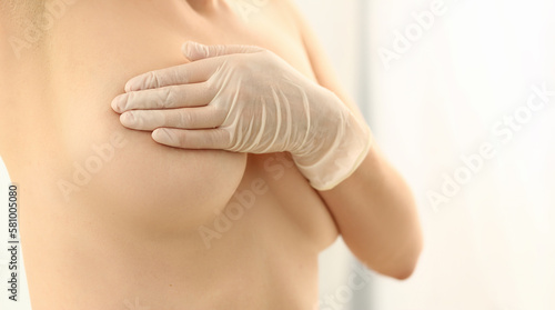 Naked woman examines breasts in gloved hands