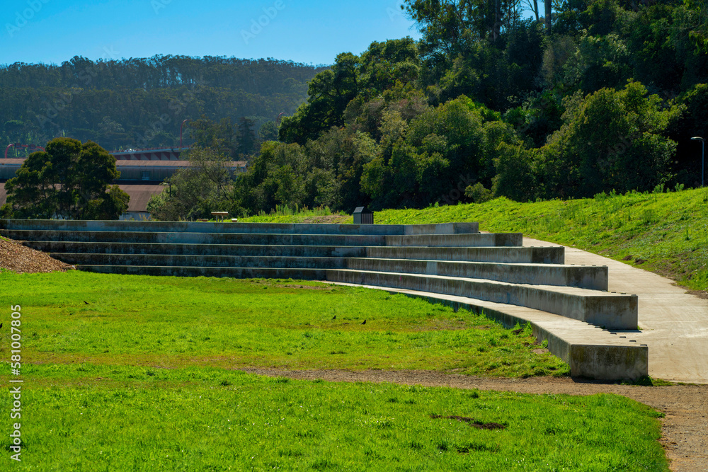 Open park or auditorium area with grass and natural background trees on mountains and blue sky in afternoon sun