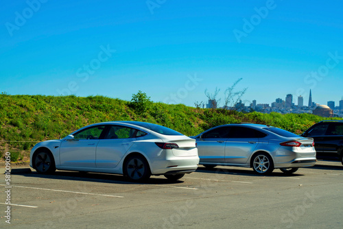 Electric vehicles in parking lot with large shrubs in late afternoon sunlight with hazy white copy space blue sky