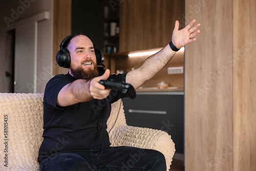 Male playing on PlayStation with the controller in his hands and with headsets on. Face expression of a gamer.