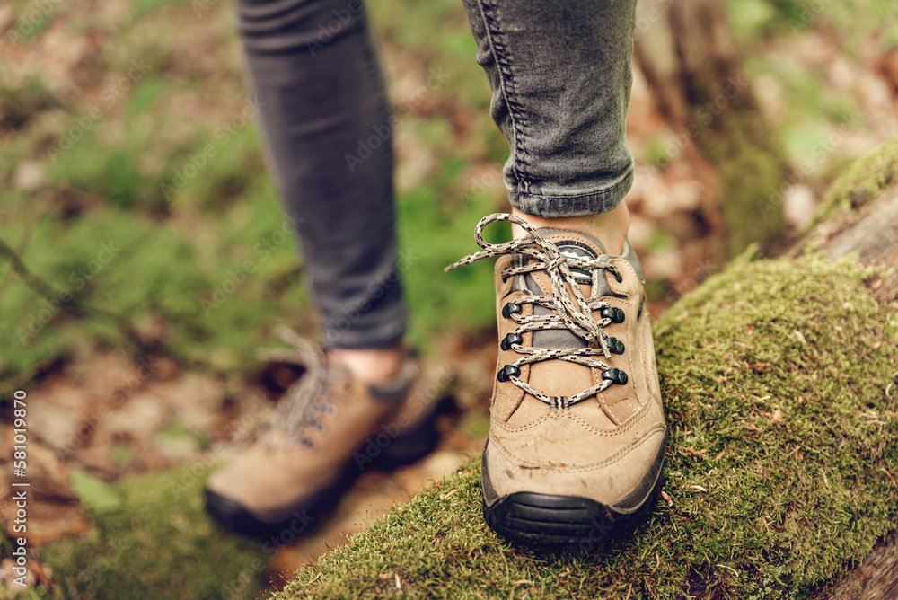 Woman wearing trekking shoes on a trail. Close up of hiker feet and hiking boots on wood log in forest. 