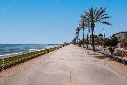 Stunning view of the promenade on backdrop of the sea, blue sky and palm trees and tourist bungalows on a sunny warm summer day. Concept of beach area in a southern country during holiday