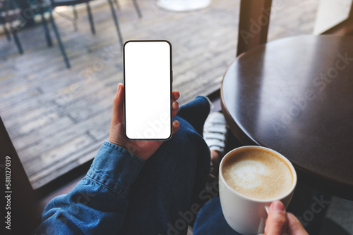 Top view mockup image of a woman holding mobile phone with blank screen and coffee cup in cafe