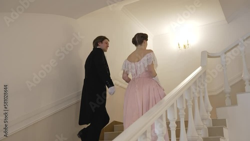 A couple in 19th century costumes. A man and a woman in 19th century costumes walk around the palace. The guy and the girl in the images of the 19th century climb the stairs. photo