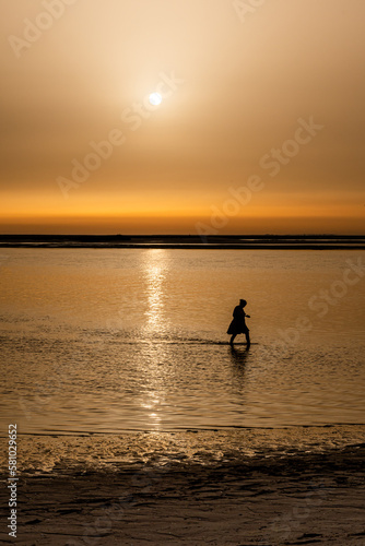 silhouette of woman walking on the beach during sunset. vertical photograph with copy space. © pulinosa