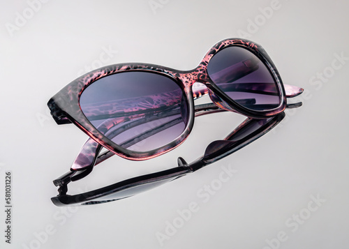 Close-up folded sunglasses in a dark purple hue with a colorful frame isolated on a light background. Horizontal. Reflection. Object shooting.
